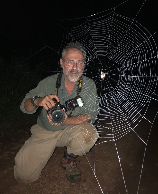 Gustavo Hormiga crouched at night beside a giant orb web, camera in hand